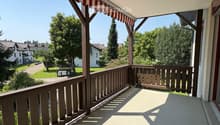wooden railing, red and white striped awning, view of a grassy area with trees and houses