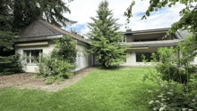 Two-story house with a pitched roof, surrounded by greenery and a well-maintained lawn.