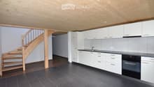 Modern kitchen with white cabinets, dark countertops, and a black tiled floor. Features a wooden staircase leading upwards.