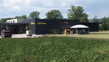 Modern commercial building with a black facade, signage for "Neff AG" and "Tenne Grill", outdoor seating area, and a grassy lawn in front.