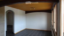 Empty room with white walls, dark tiled floor, wooden ceiling beams, and a window with blinds.