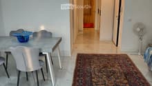 Modern hallway with marble flooring, a patterned rug, and a dining area visible to the left, featuring a grey table, chairs, and a decorative bowl.