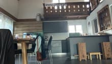Modern kitchen with wooden table, chairs, stools, grey cabinets, and a wooden balcony railing above.