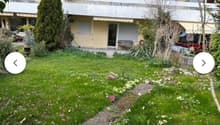 Well-maintained garden with green lawn, colorful flowers, shrubs, and a small bench near the building entrance.