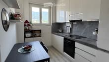 Modern kitchen with white cabinets, dark countertops, and a dining area featuring a table and chairs. The kitchen includes an oven, sink, and various appliances.