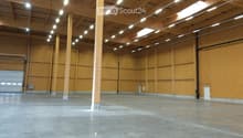 Empty warehouse space with wooden walls, concrete floor, exposed wooden beams, and a large garage door.
