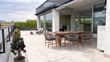 Modern rooftop terrace with a wooden dining table, six chairs, a lounge chair, a small side table, and a potted tree.