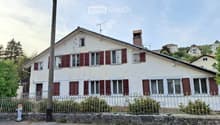 Two-story white house with red shutters, multiple windows, chimney, and a small garden behind a metal fence.