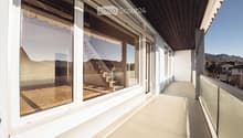 Spacious balcony with large windows, wooden flooring, and a view of the surrounding landscape.
