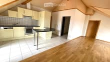 Bright, modern kitchen with light-colored cabinets, stainless steel appliances, and a central island. The space features a mix of tiled and wooden flooring, with a doorway leading to another room.