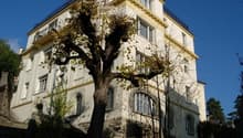 A multi-story building with a balcony on the top floor, surrounded by trees.