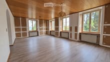 Empty room with wooden flooring and wooden ceiling, large windows with radiators below, and exposed wooden beams on the ceiling.
