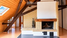 Modern living room with exposed wooden beams, skylight, and a brick fireplace with tools nearby.