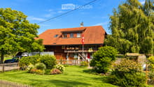 Two-story house with red-tiled roof, wooden balcony, and well-maintained garden with a wooden fence.