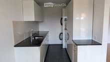 Modern kitchen with white cabinets, black countertops, stainless steel sink, and a washing machine in the background.