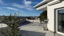 Modern rooftop terrace with tiled floor, small table and chairs, potted plants, and a view of the city and mountains.