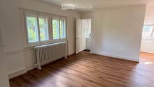 Empty room with wooden flooring, white walls, large windows, radiator, and a door leading to another room.
