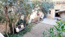 a cozy garden with bench, trees, greenery, stone pathways, and stone house in the background