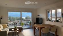 Modern living and dining area with a view, featuring a grey sectional sofa, coffee table, dining table with chairs, and a television.
