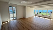 Empty room with wooden flooring, large windows, and a sliding glass door leading to a balcony.