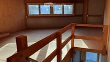 Empty wooden loft space with exposed beams, wooden floor, and large windows allowing natural light. No furniture or furnishings present.
