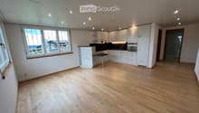 Empty room with light wooden flooring, white walls, and white cabinetry. Large windows provide natural light, and the space is unfurnished.