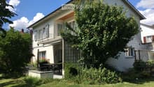 Two-story white house with a balcony, surrounded by a well-maintained garden and lawn.
