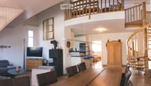 Open-plan living and dining area with a fireplace, television, sofa, coffee table, dining table with chairs, and a kitchen area with stools.