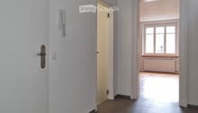 Empty hallway with tiled floor, white walls, and two doors leading to other rooms. One door has a visible telephone and light switch.