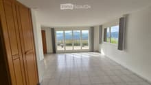 Empty hallway with tiled floor, white walls, large windows, and sliding glass doors leading to an outdoor area.