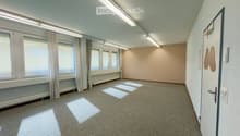 Empty room with carpeted floor, large windows with curtains, and a door. No furniture or equipment present.