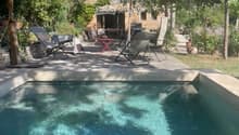 Outdoor patio area with a swimming pool, lounge chairs, umbrella, and a stone house in the background.