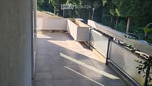 Balcony with tiled floor, modern railing, and a view of greenery and parked cars.