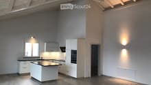 Modern kitchen with white cabinets, a central island, and built-in appliances, featuring large windows and warm lighting.