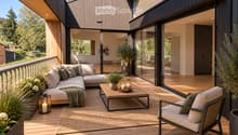 Modern outdoor balcony with wooden decking, a sectional sofa, coffee table, armchair, lantern, and potted plants.