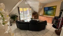 Bright living room with a black sectional sofa, coffee table, wooden cabinet, and a fireplace. Large windows offer a view of the garden and pool.