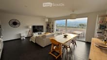 Modern living and dining area with a sofa, dining table, chairs, television, shelves, and a large window offering a scenic view.