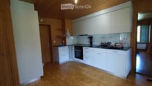 Modern kitchen with white cabinets, wooden flooring, and a black countertop. Features an oven, sink, and various kitchen items including a dish rack and bottles.