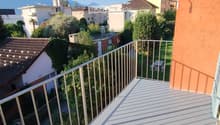 Balcony with metal railing, overlooking a residential area with houses, trees, and a clear blue sky.