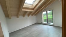 Empty attic space with wooden slanted ceilings, skylight windows, and large sliding glass door opening to outdoor view.