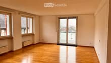 Empty room with wooden flooring, large windows, and a sliding glass door leading to a balcony.