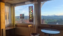Bright room with large windows offering a scenic mountain view, featuring a wooden chair, a round glass table, and decorative curtains.