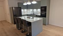 Modern kitchen with grey cabinets, marble countertops, stainless steel appliances, and pendant lights above the island.