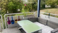 Balcony with a green table, wicker sofa, and hanging flower pots.