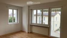 Empty room with wooden flooring, large windows, radiator, and a sliding glass door leading to a balcony.