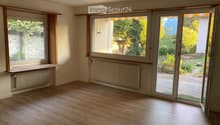 Empty room with wooden flooring, large windows, radiators, and sliding glass doors opening to a garden.