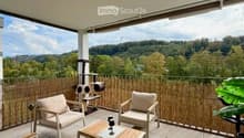 Balcony with a scenic view of a forested area, featuring a tiled floor, a bamboo privacy screen, and a small seating area with chairs and a coffee table.