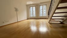 Empty room with wooden flooring, large windows, and a staircase leading upwards.