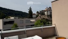 Rooftop terrace with white sofa, coffee table, small table with a bowl, and a decorative fire pit, overlooking a scenic town and castle.