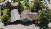 Aerial view of a two-story house with a gray roof and multiple chimneys, surrounded by trees and neighboring houses.